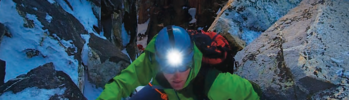 A climber wearing a SureFire headlamp ascending a snow-covered rock face at dusk, photographed during a SureFire shoot