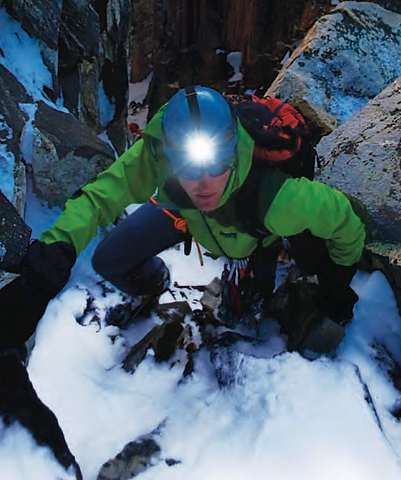 Climber with headlamp ascending a snowlit rock face