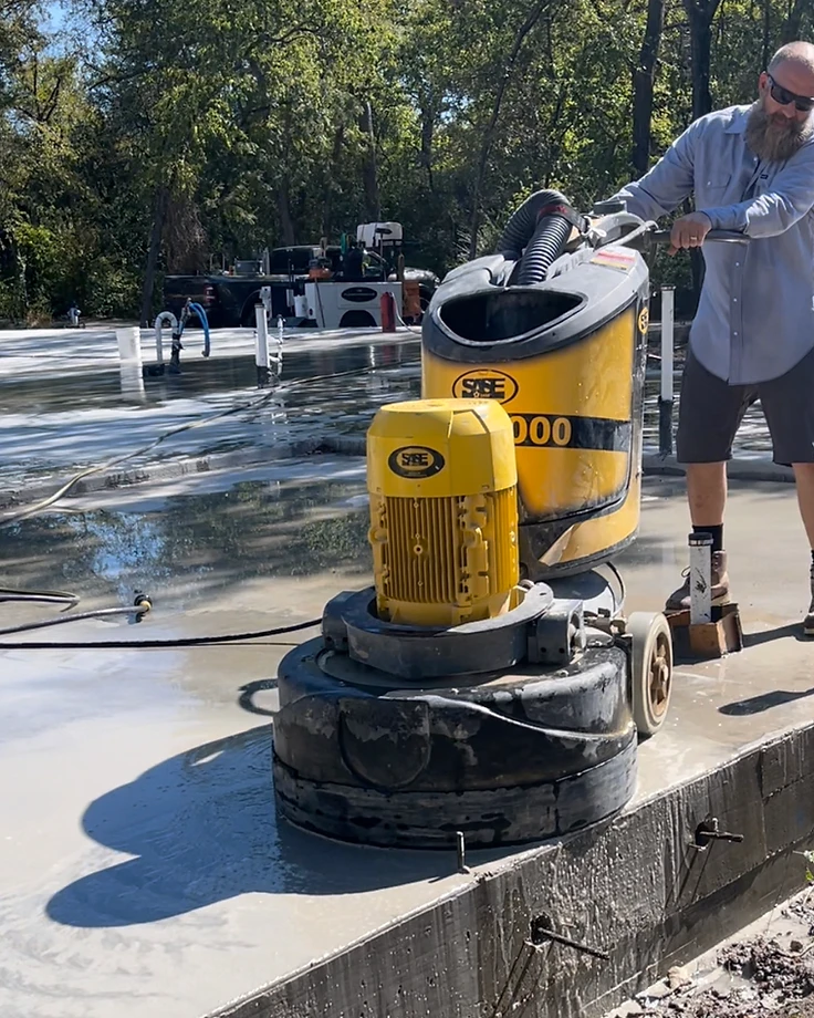 Jeremy Redig running a grinder on a wet concrete slab — real FloorRescue jobsite work