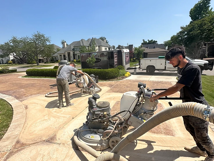Two FloorRescue installers grinding a concrete driveway with industrial floor grinders and vacuum equipment on a residential job site