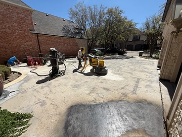 Worker operating a yellow PDG 8000 concrete grinder across a residential driveway