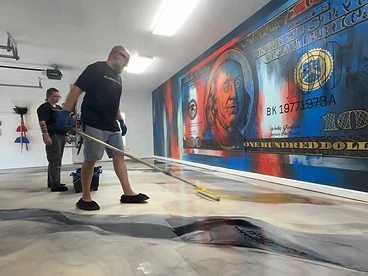 Installer rolling a metallic epoxy topcoat across a wet, swirling garage floor