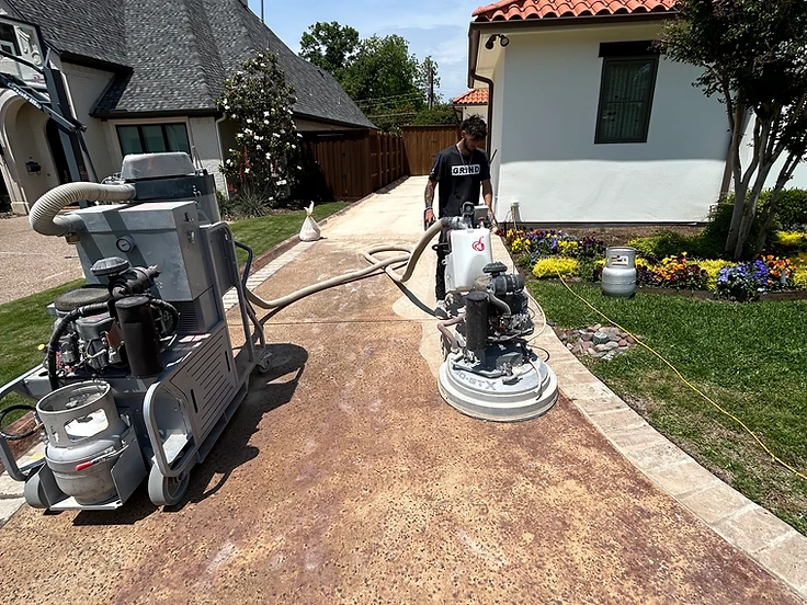 Installer actively grinding a concrete driveway with a walk-behind floor grinder and dust collection system