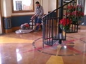 Installer operating a walk-behind concrete polishing machine on a polished concrete floor with a compass-rose inlay