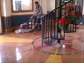 Installer operating a walk-behind concrete polishing machine on a polished concrete floor with a compass-rose inlay