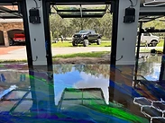 Completed metallic epoxy garage floor — vibrant blue, green, and amber marbled finish viewed through the open glass door