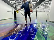 Worker applying product with a pressurized sprayer across the wet floor during a metallic epoxy installation