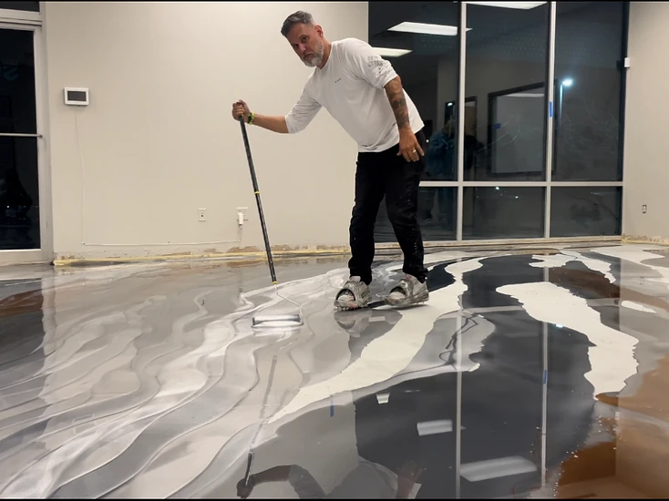 Installer wearing spiked shoes rolling a metallic epoxy coating on a full-size floor during hands-on training