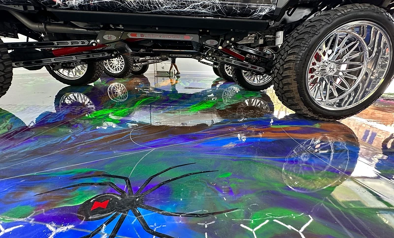 Custom lifted Black Widow truck parked on a metallic epoxy floor with royal blue, green, and bronze pigments and a hand-painted black widow spider inlay