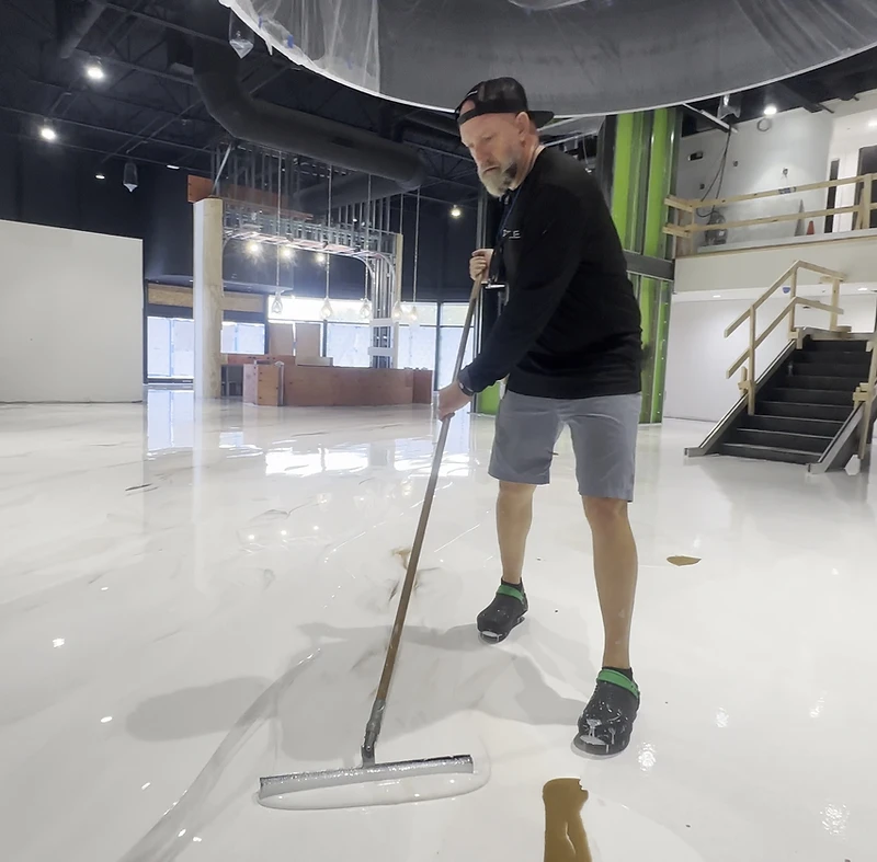 Jeremy spreading a white metallic epoxy floor with a crew member behind him