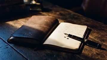An open leather notebook and fountain pen in a beam of golden light