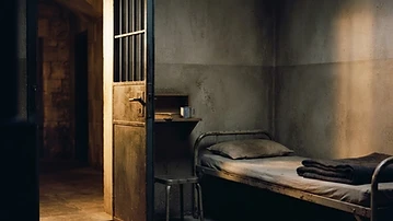 A modest cell with its door open and soft evening light