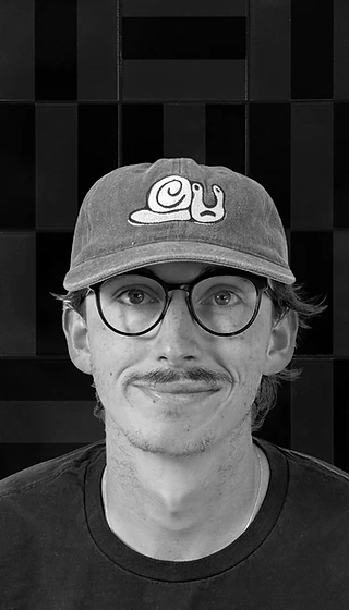 Black-and-white portrait of Jake, co-founder and photographer, wearing a cap and glasses