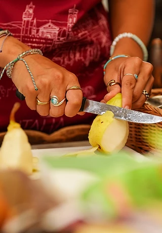 A pair of hands slicing a pear on a board in a sunlit kitchen — the everyday made careful