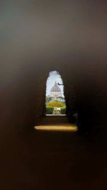 A distant domed basilica glimpsed through a dark keyhole — the gap, opened