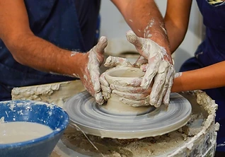 Two pairs of hands shaping wet clay on a pottery wheel — a lesson in the round