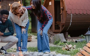 Gathering around a fire pit beside a barrel sauna at dusk