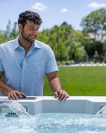 Homeowner tending to a hot tub with active water features on a sunny lawn