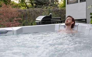 Man relaxing with eyes closed in a bubbling white hot tub at golden hour