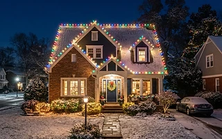 Suburban home at night outlined in warm holiday string lights