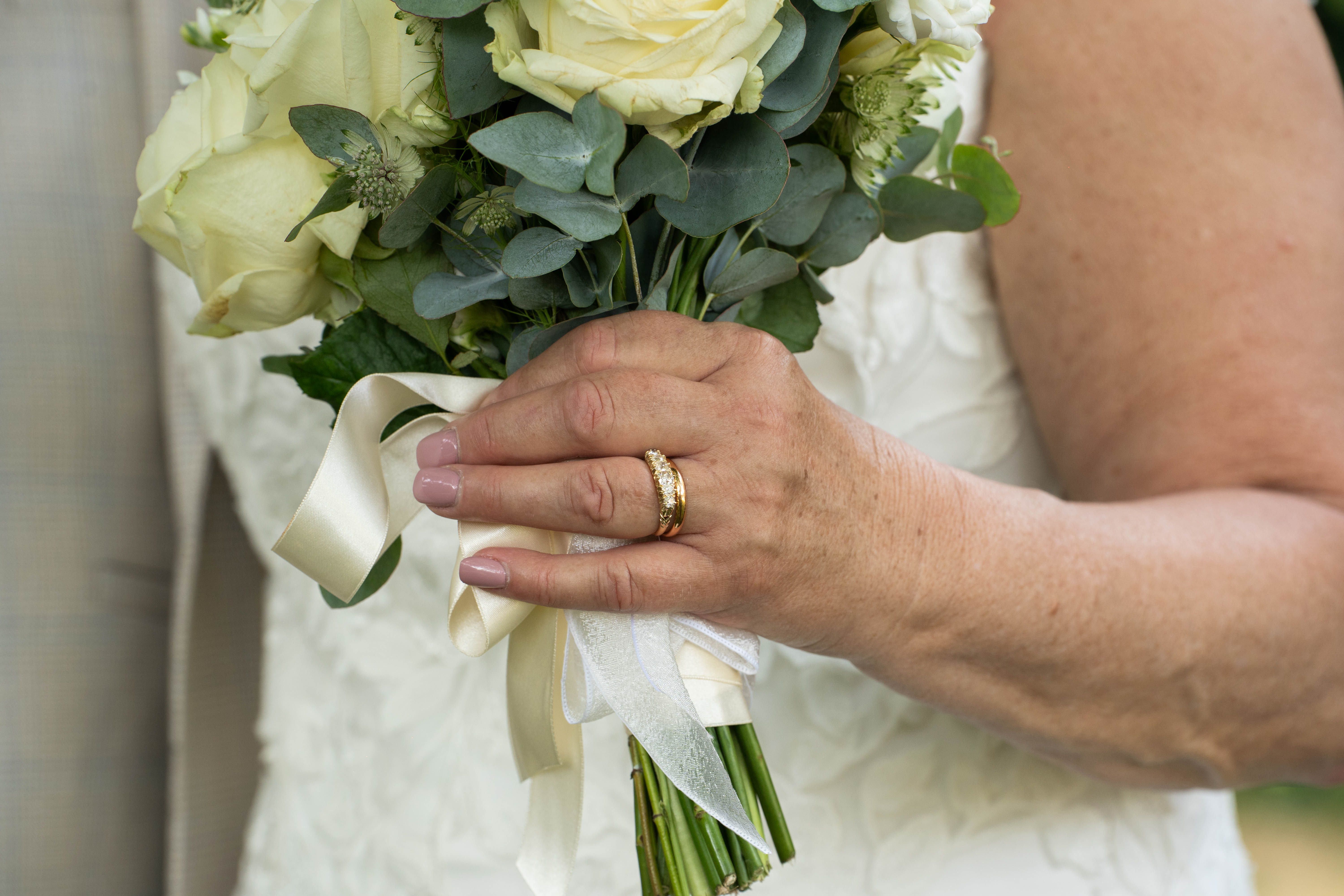 Detail shot of the bride's hand holding a bouquet of white roses and eucalyptus with ivory ribbon