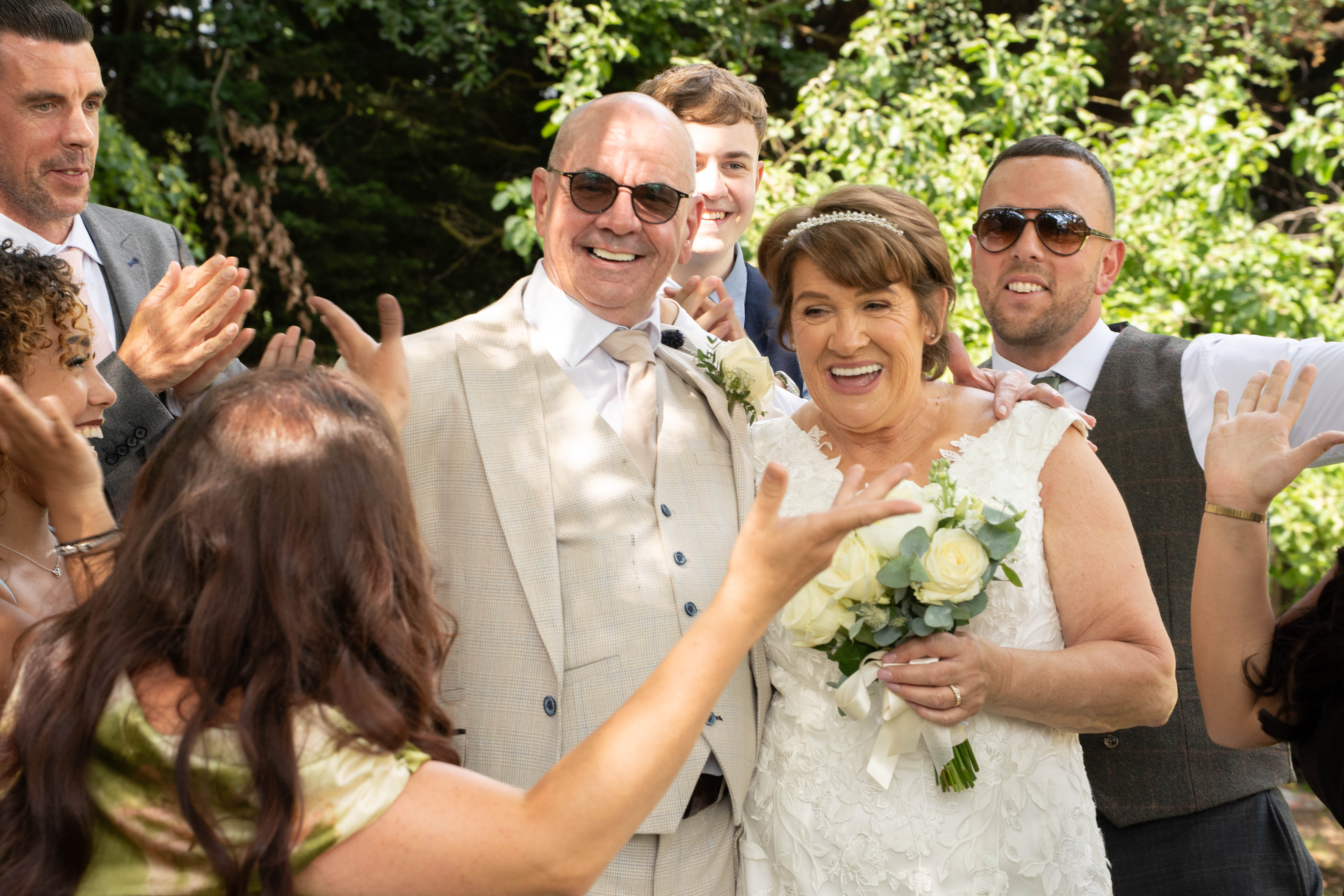 Sheila and John surrounded by cheering family members in a woodland setting
