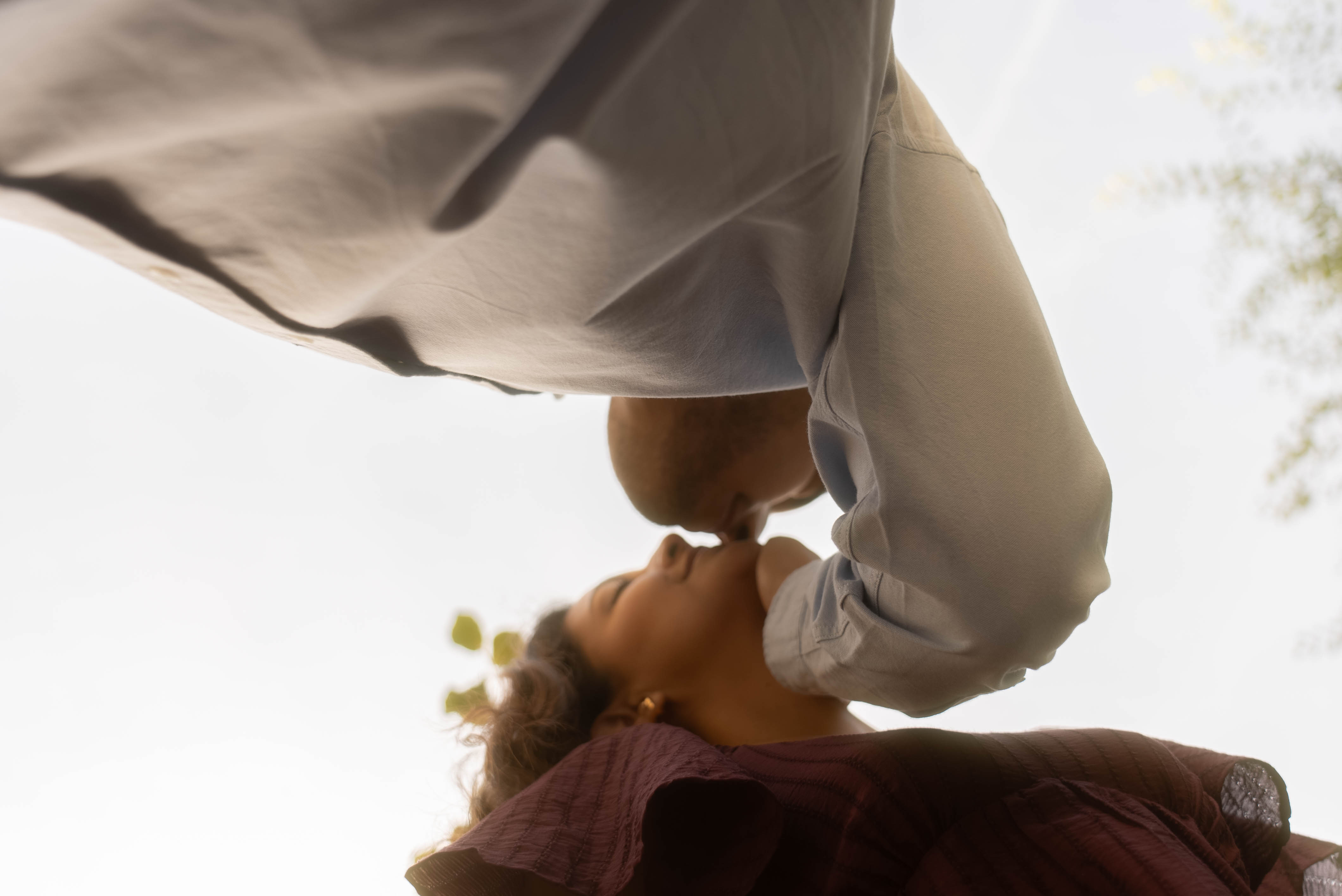 Low-angle shot of the couple leaning in for a kiss against a bright golden sky