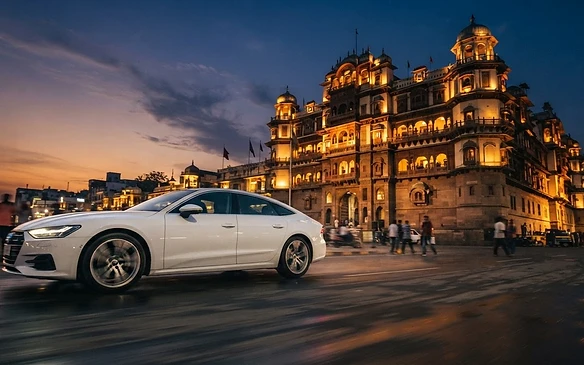 Premium sedan passing Rajwada Palace in Indore at dusk