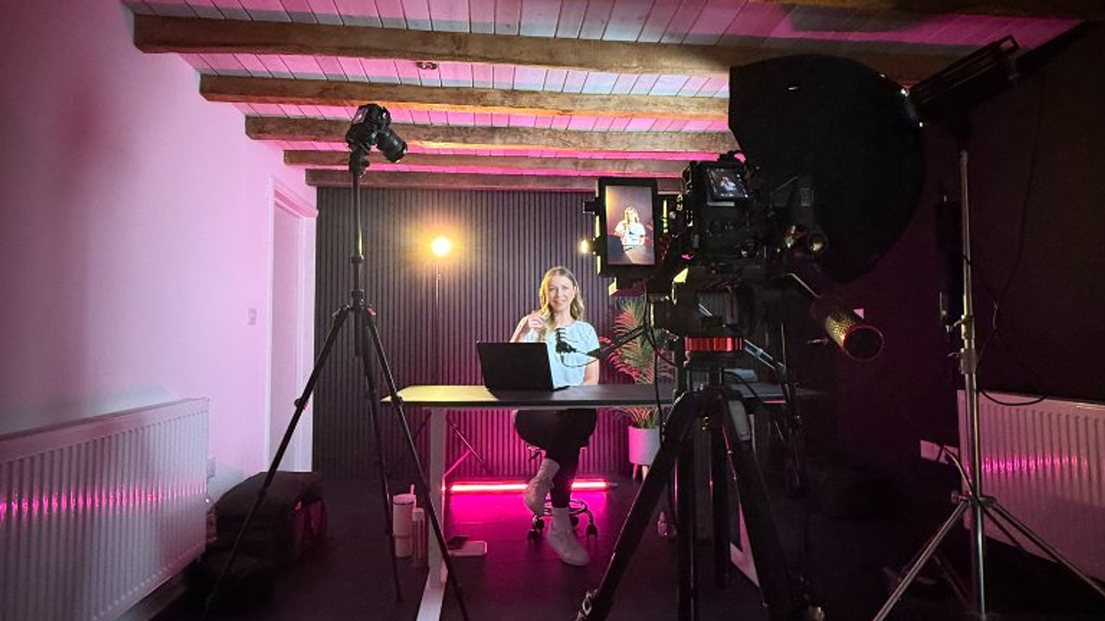 Behind the scenes on the Modash studio shoot, presenter at the desk under pink lighting with the camera rig in shot