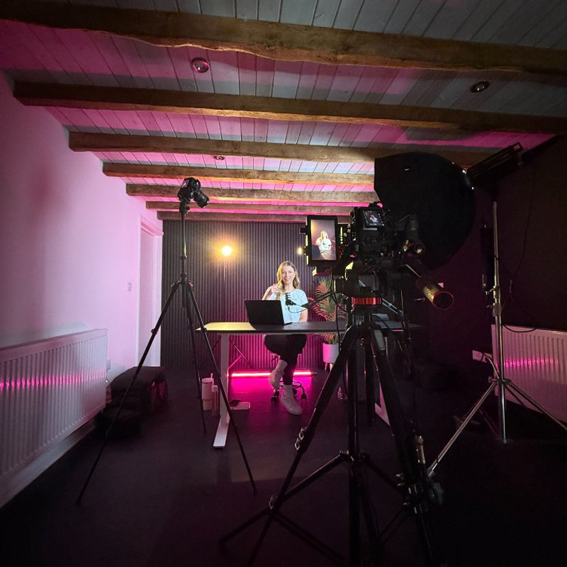 Behind the scenes on the Modash studio shoot, presenter at the desk under pink lighting with the camera rig in shot