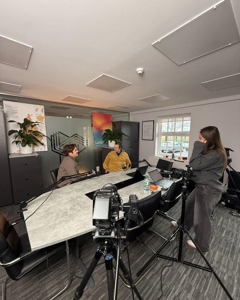 Two-person interview setup on the Landstack shoot, camera in the foreground and the Landstack poster on the wall behind