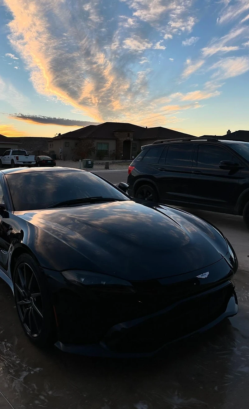 Glossy black Aston Martin Vantage at sunset, full vehicle in frame