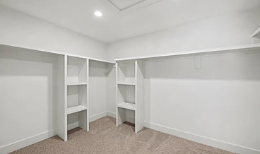 Walk-in closet with white laminate shelving, hanging rods, and beige carpet