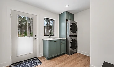 Laundry room with sage cabinetry, stacked washer and dryer, and a utility sink
