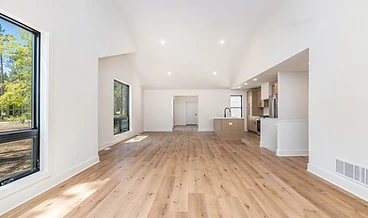 Open-concept living room opening to the kitchen, vaulted ceilings and wide-plank floors