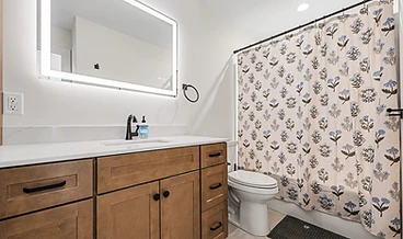 Bathroom with a wood vanity, matte black faucet, and an LED-backlit mirror
