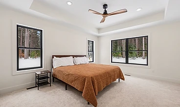 Primary bedroom with a rust quilted bedspread and black-framed windows onto the snow