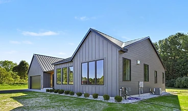 Modern gray home with a dark metal roof and a manicured lawn