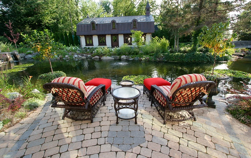 Coin détente sur une terrasse en pavé au bord d’un bassin dans un jardin verdoyant