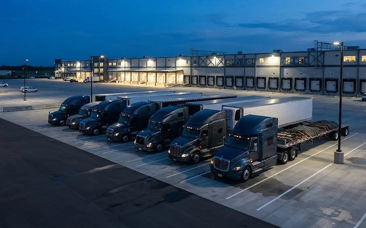 Row of modern semi-trucks at a logistics facility at blue hour
