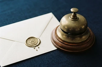 Ivory envelope with a gold wax seal beside a brass desk bell