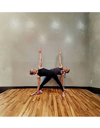 Two members balancing in a yoga pose against a studio wall