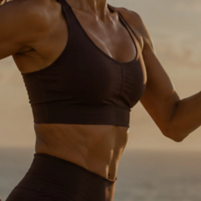 A woman in her forties running along a beach at sunset