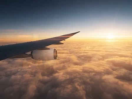 Airplane wing above golden clouds at sunrise
