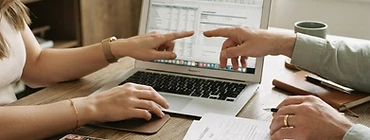 Two pairs of hands working on a laptop with a calculator and loan documents