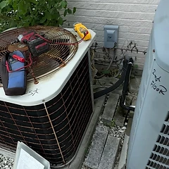 Outdoor AC condenser serviced against a brick wall with tools on the fan grille