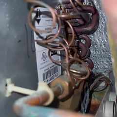 Close-up of an evaporator coil and copper lines with a unit serial-number plate