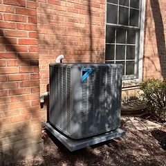 Daikin AC condenser installed on a pad beside a brick home