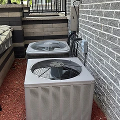 Dual central AC condenser installation against a brick wall