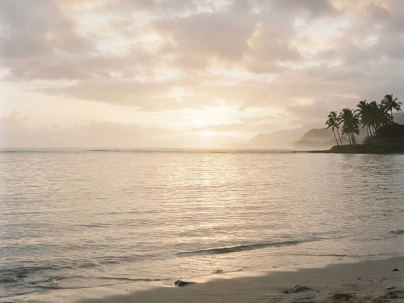 A serene Hawaiian seascape at dawn, golden light breaking through morning clouds over a calm ocean